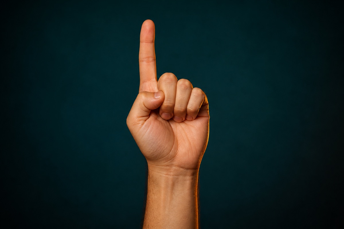 Right hand with one index finger raised against a dark teal studio background